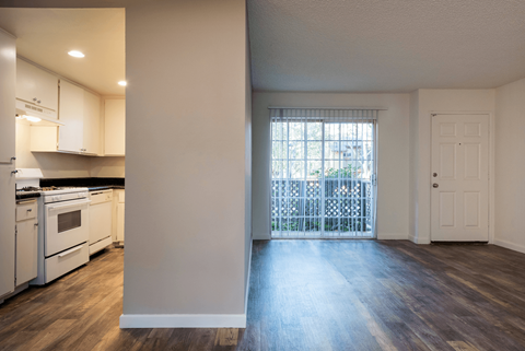 Kitchen with White Appliances and White Painted Cabinets viewed from Living Area with Patio and Entryway Visible